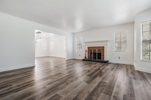 unfurnished living room featuring dark wood-type flooring, a brick fireplace, a notable chandelier, and baseboards