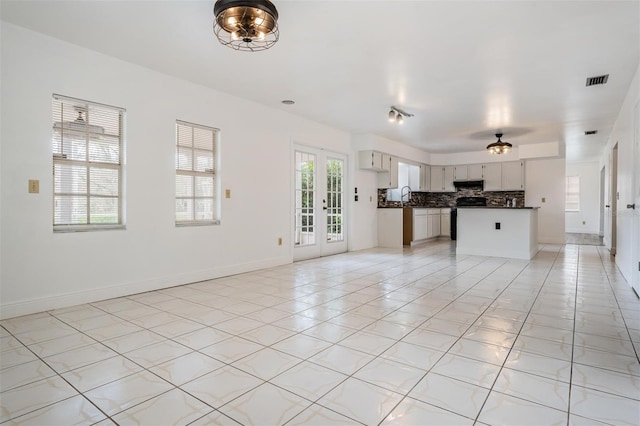 unfurnished living room featuring light tile patterned floors, baseboards, visible vents, a sink, and french doors