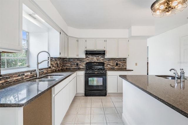 kitchen featuring black gas stove, dark stone countertops, under cabinet range hood, and a sink