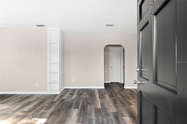 spare room with built in shelves and dark wood-type flooring