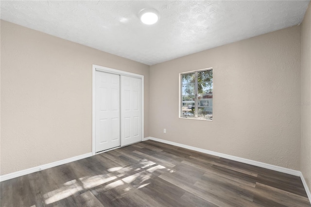 unfurnished bedroom with a textured ceiling, dark wood-type flooring, and a closet