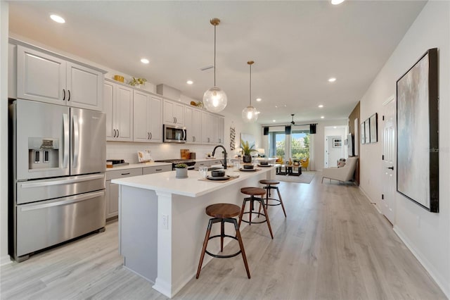 kitchen with appliances with stainless steel finishes, a kitchen breakfast bar, a center island with sink, decorative light fixtures, and light hardwood / wood-style floors