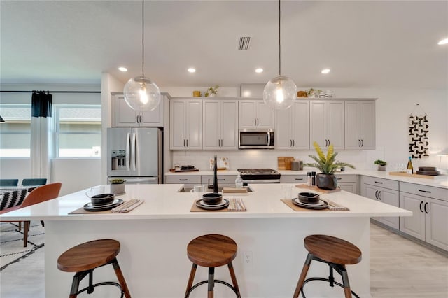 kitchen featuring a breakfast bar, a center island with sink, gray cabinets, and appliances with stainless steel finishes