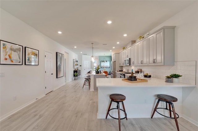 kitchen featuring a kitchen bar, kitchen peninsula, stainless steel appliances, and light hardwood / wood-style floors