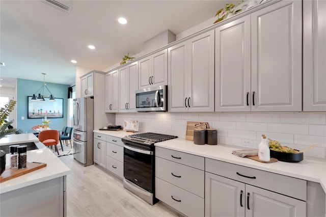 kitchen with gray cabinetry, decorative backsplash, light wood-type flooring, decorative light fixtures, and stainless steel appliances