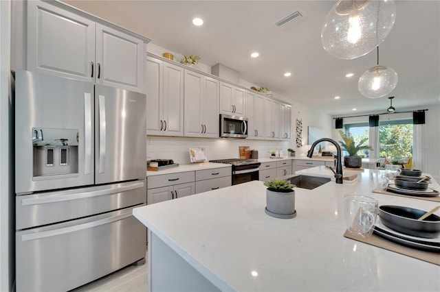 kitchen with sink, light stone countertops, appliances with stainless steel finishes, tasteful backsplash, and decorative light fixtures