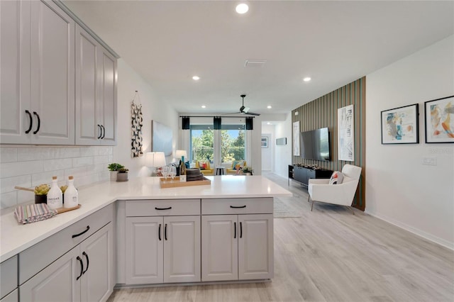 kitchen featuring kitchen peninsula, backsplash, ceiling fan, light hardwood / wood-style flooring, and gray cabinets