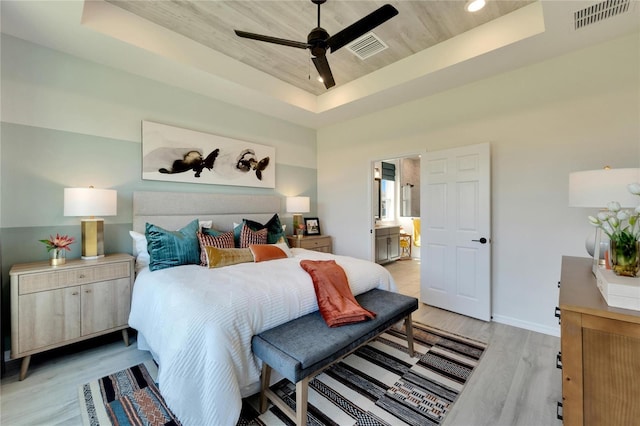 bedroom with ceiling fan, a raised ceiling, ensuite bathroom, and light hardwood / wood-style flooring