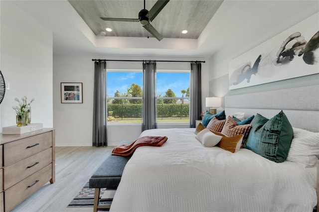 bedroom with a raised ceiling, ceiling fan, and light wood-type flooring