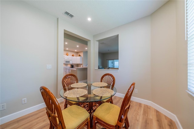 dining room with a textured ceiling, a wealth of natural light, and light hardwood / wood-style flooring