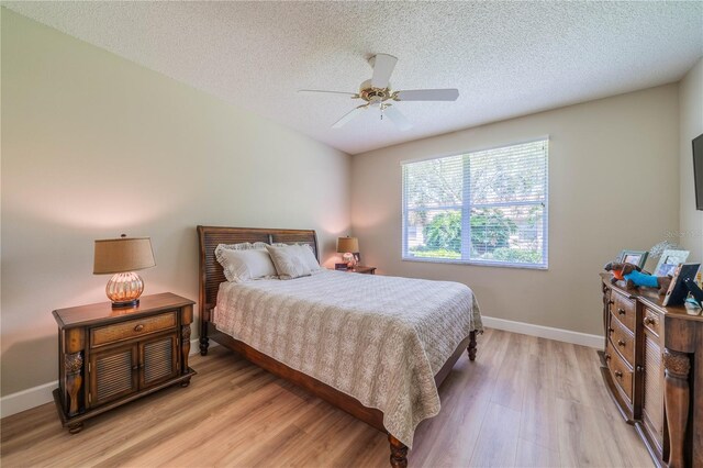 bedroom with ceiling fan, light wood-type flooring, and a textured ceiling