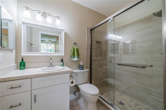 bathroom featuring ceiling fan, a textured ceiling, an enclosed shower, toilet, and vanity