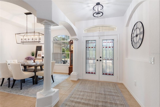 foyer featuring a notable chandelier, french doors, decorative columns, and light tile flooring