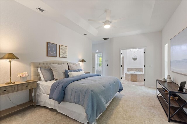 bedroom featuring light carpet, a tray ceiling, connected bathroom, and ceiling fan