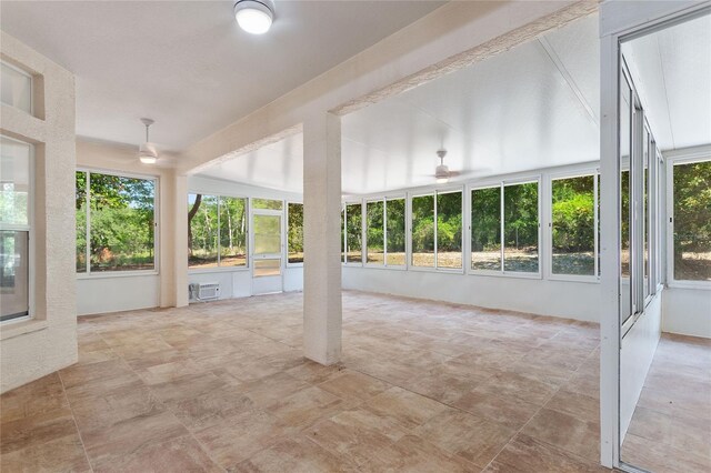 unfurnished sunroom with ceiling fan, a wealth of natural light, and a wall mounted AC