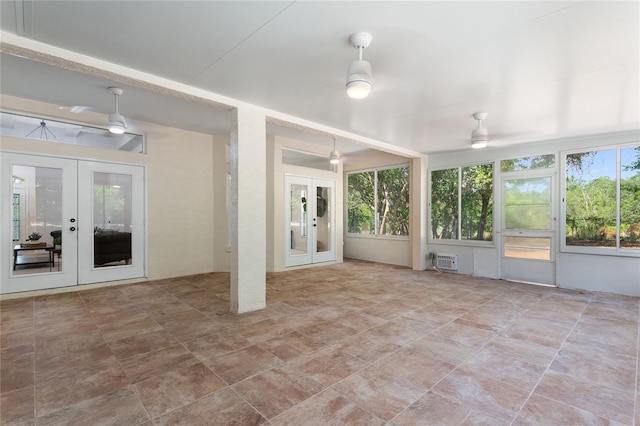 unfurnished sunroom with a wall unit AC, plenty of natural light, ceiling fan, and french doors