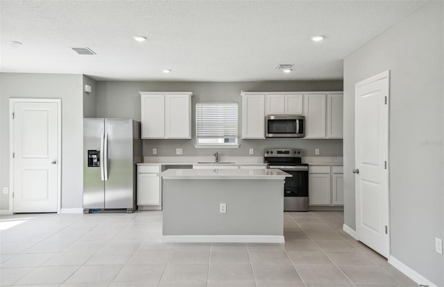 kitchen with appliances with stainless steel finishes, sink, white cabinets, a kitchen island, and light tile patterned flooring