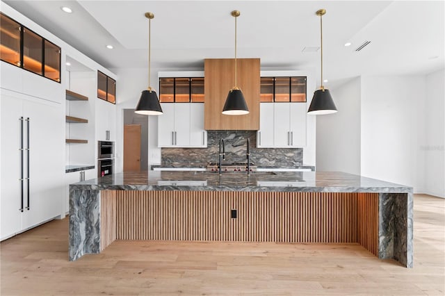 kitchen featuring a spacious island, open shelves, light wood-style flooring, decorative backsplash, and pendant lighting