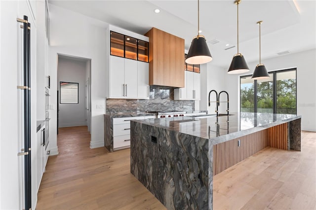 kitchen with a sink, decorative backsplash, light wood-style flooring, and dark stone countertops