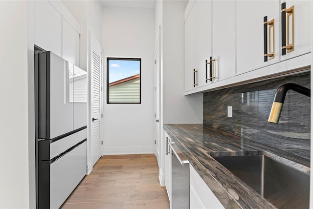 kitchen with tasteful backsplash, freestanding refrigerator, light wood-style floors, white cabinetry, and a sink