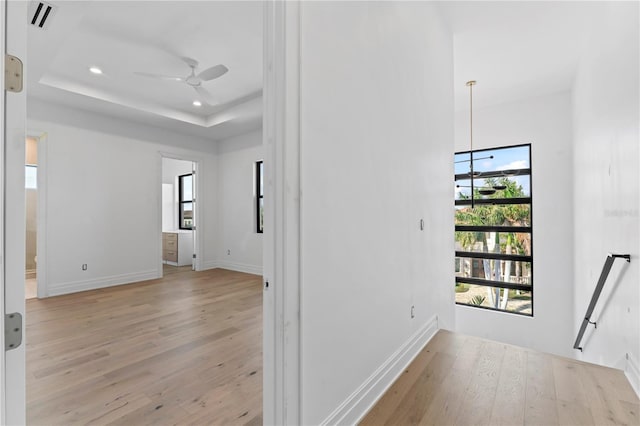 hall with visible vents, baseboards, light wood-style flooring, recessed lighting, and a raised ceiling