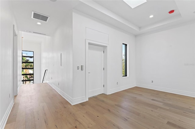 interior space featuring a raised ceiling, light wood-style flooring, baseboards, and visible vents