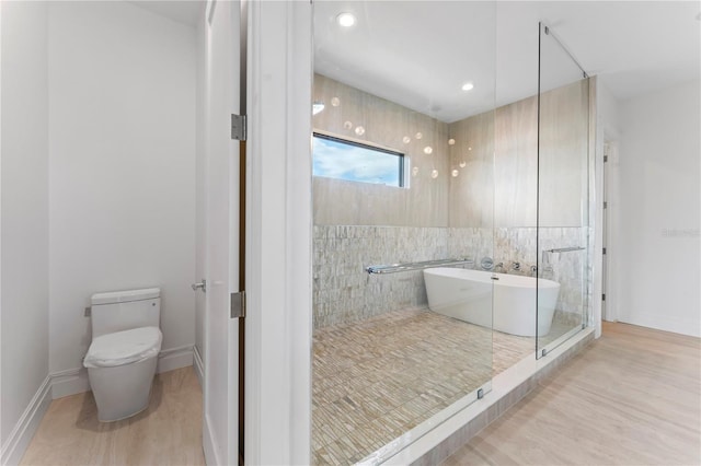 bathroom featuring baseboards, toilet, a freestanding bath, recessed lighting, and wood finished floors