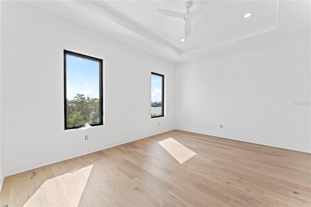 spare room featuring baseboards, light wood-style flooring, recessed lighting, ceiling fan, and a raised ceiling