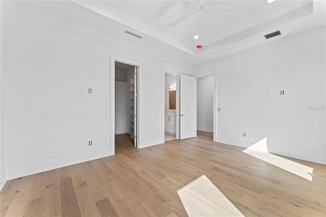 unfurnished bedroom with a walk in closet, a tray ceiling, light wood-style floors, and visible vents