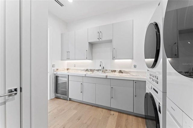 kitchen featuring visible vents, beverage cooler, light wood-style floors, light countertops, and stacked washer / dryer