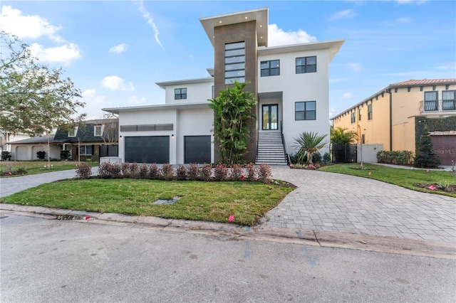 contemporary house featuring a garage, stucco siding, decorative driveway, and a front yard