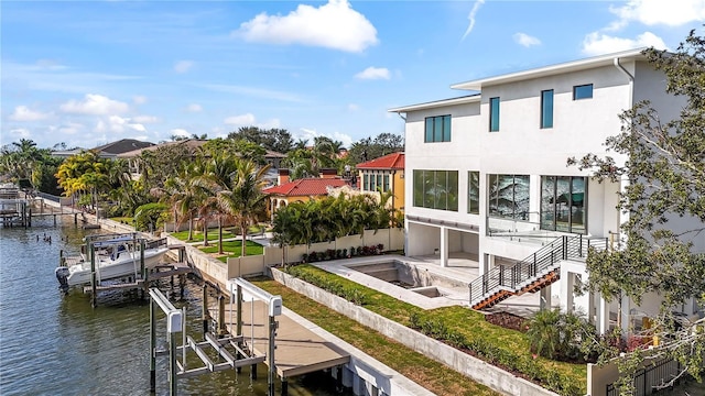 back of house with fence, a water view, stairway, stucco siding, and boat lift