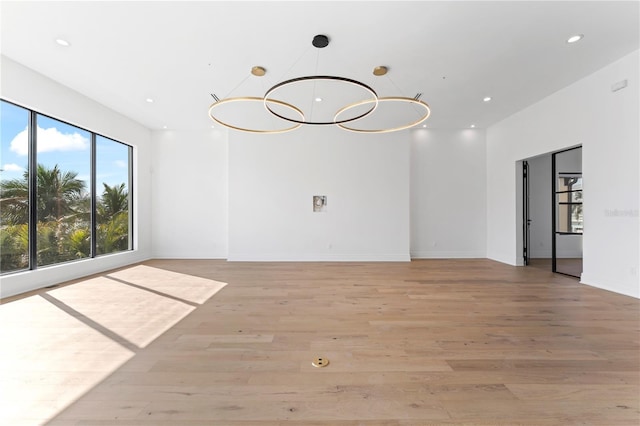 empty room with a notable chandelier, recessed lighting, baseboards, and light wood-style floors