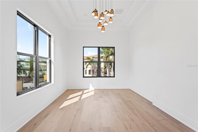 unfurnished room with a notable chandelier, a healthy amount of sunlight, a raised ceiling, and light wood-style floors