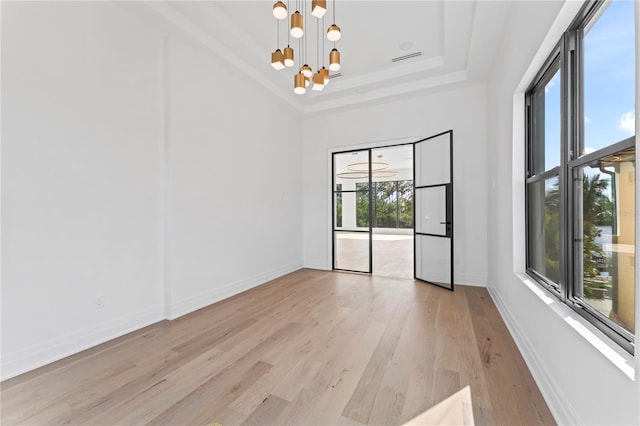 empty room with a notable chandelier, baseboards, light wood-style floors, and a raised ceiling