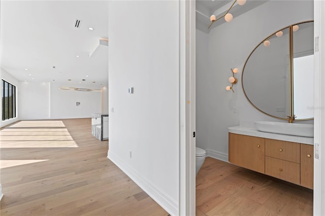 hallway featuring a sink, baseboards, recessed lighting, and light wood finished floors