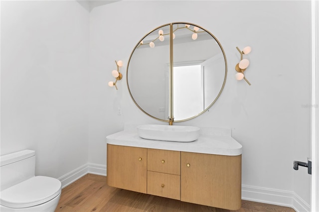 half bathroom with baseboards, toilet, wood finished floors, and vanity