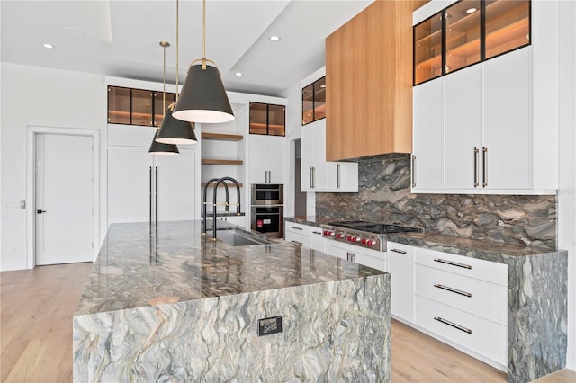 kitchen with a sink, backsplash, appliances with stainless steel finishes, and light wood finished floors