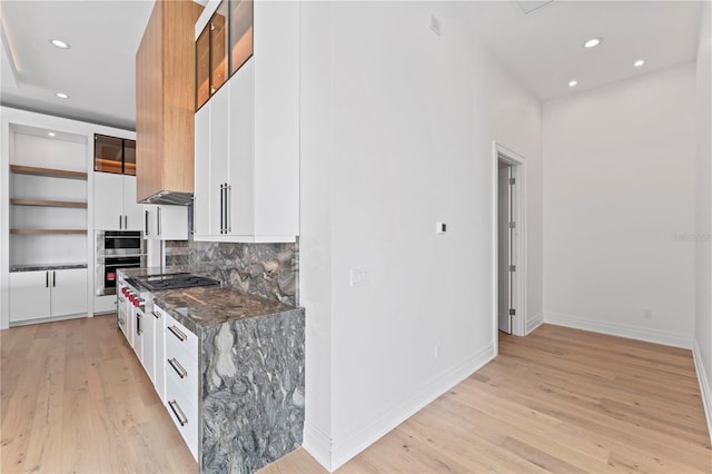 kitchen with light wood finished floors, dark stone counters, recessed lighting, white cabinets, and tasteful backsplash