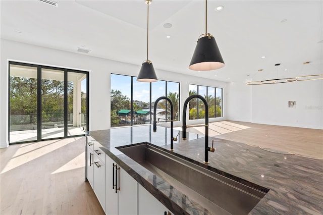 kitchen featuring light wood finished floors, decorative light fixtures, recessed lighting, white cabinets, and a sink