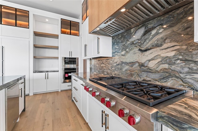 kitchen with custom range hood, decorative backsplash, light wood-style flooring, appliances with stainless steel finishes, and open shelves