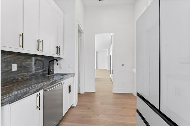 interior space featuring tasteful backsplash, baseboards, dishwasher, light wood-style floors, and a sink