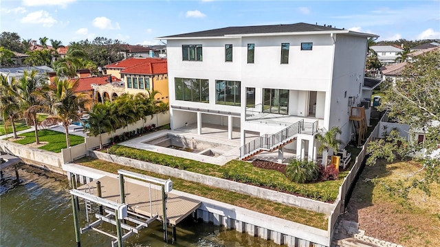 back of property featuring a fenced backyard, stucco siding, a water view, boat lift, and a patio area