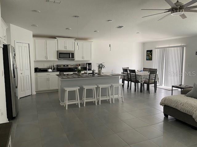 kitchen featuring white cabinetry, hanging light fixtures, an island with sink, a breakfast bar, and appliances with stainless steel finishes