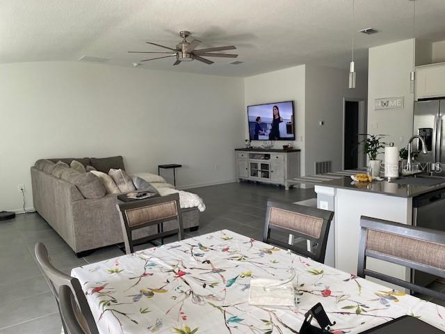 living room with ceiling fan, light tile patterned flooring, and lofted ceiling