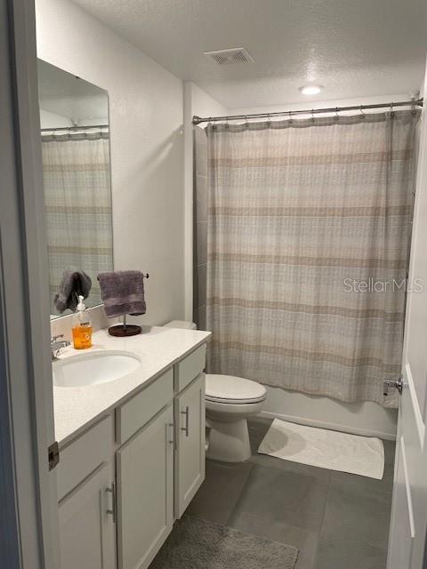 full bathroom featuring vanity, tile patterned flooring, toilet, shower / bathtub combination with curtain, and a textured ceiling