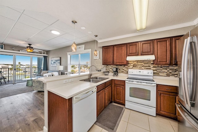 kitchen with a sink, a peninsula, open floor plan, under cabinet range hood, and white appliances