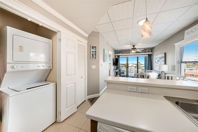 clothes washing area with light tile patterned floors, a sink, stacked washer / dryer, a ceiling fan, and laundry area
