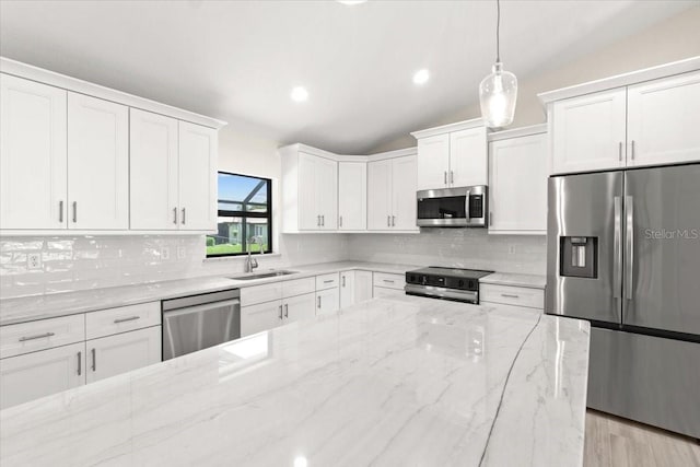 kitchen with appliances with stainless steel finishes, decorative light fixtures, vaulted ceiling, white cabinets, and sink