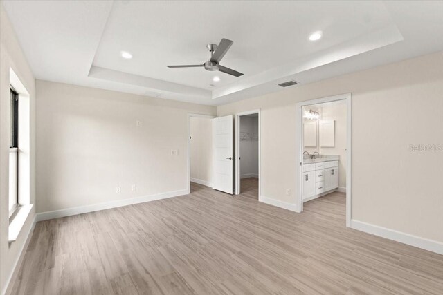 unfurnished bedroom featuring a spacious closet, a closet, a raised ceiling, ceiling fan, and ensuite bathroom